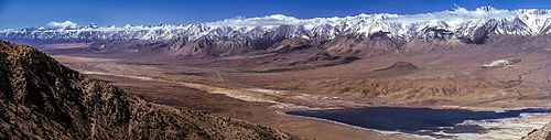 Wide-format image of a high plain, mostly unvegetated, with snow-capped mountains in the background
