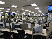A large room with a suspended ceiling packed with cubicles containing computer monitors