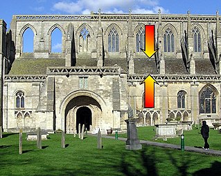 Malmesbury Abbey, showing the location of the triforium. It lies between the lower (aisle) windows and the upper (clerestory) windows, as arrowed. It is shallow, as it is inside the roofspace of the side aisles.