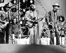 The Beach Boys performing on stage with an array of backup musicians. From the group, Al Jardine, Carl Wilson, and Mike Love are pictured.
