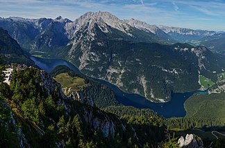 Die zentralen Gratgebirge von Watzmann und Hochkalter vor den Hochflächen bildenden Stöcken des Steinernen Meeres und der Reiter Alm. Quer durch das Bild zieht sich der Königssee.