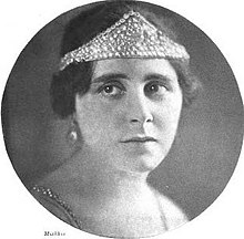A white woman with dark hair, wearing a jeweled tiara across her forehead.