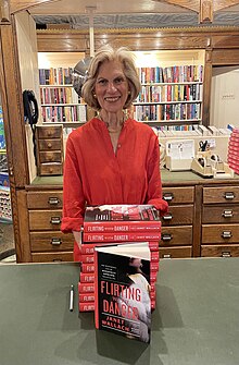 A woman in a red dress stands in a bookstore with a stack of books ahead of her.