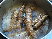 Several knobby elongated light brown tubers in a pot with water