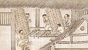 Five men prepare boards with embedded twigs, which are placed face-down on a raised frame.