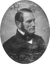A black-and-white head-and-shoulders photographic portrait of Parkman. He faces to the right, sports long sideburns, and wears a dark suit and tie. The photograph has scratches and other damage.