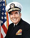 man in Navy uniform with cap, American flag in background