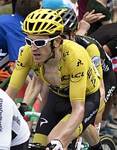 Geraint Thomas wearing a yellow jersey riding amongst other riders