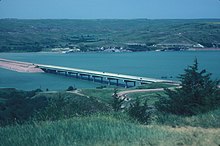 Distant view of a simple highway bridge crossing a wide river surrounded by rolling hills free of vegetation