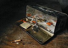 A black metal box turned on its side and opened to show instruments used for heroin use, including a silver spoon and syringes