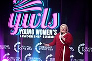 Kat Cammack addressing the Young Women's Leadership Summit 2022 in Grapevine, Texas. She's wearing a red dress and is talking into a microphone.