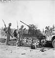 Black Watch soldiers pass by a burning German anti-aircraft half-track, Sicily, 5 August 1943.