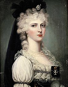 A young woman in an ornate black-and-white Hungarian-style dress. Her hair, powdered white, is decorated with black ribbons and veil.
