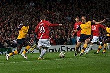Wayne Rooney (in red) is shaping to kick the ball with an Arsenal player (in yellow) on either side of him. Cristiano Ronaldo, Carlos Tevez (both Manchester United) and Kolo Touré (Arsenal) are looking on in the background.