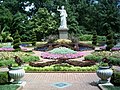 small white statue in ornate garden with right arm raised