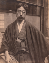 Portrait of an Asian man with moustache dressed in traditional Japanese clothes. He is looking down with his arms crossed.