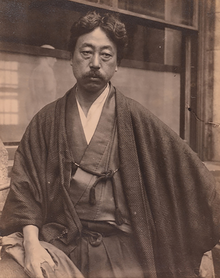 Portrait of an Asian man with moustache dressed in traditional Japanese cloths. He is looking down with his arms crossed.