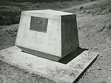 a black and white photograph of a concrete plinth with a plaque, overlooking a hill slope