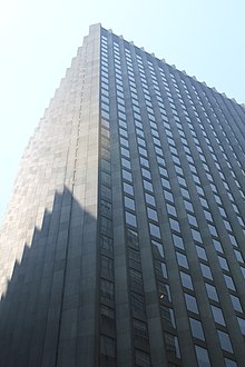 The facade of the CBS Building's upper stories, seen on a sunny day. The facade consists of angled rectangular piers, which are made of black granite. There are narrow glass windows between each pier on each stories.