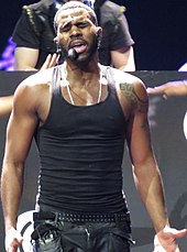 A man in a black vest during a performance with his eyes closed