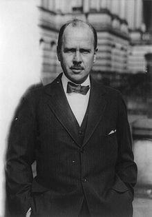 Balding man in three-piece suit, with bow-tie, stares intently at the camera.