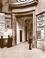 Eingang zum alten Burgtheater mit Theaterplakaten (um 1880). Der eigentliche Eingang zwischen den Kandelabern ist heute noch im Bereich der Michaelerkuppel vorhanden und mit einer Gedenkplakette versehen.