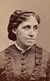 A hazy photograph of Louisa May Alcott, with dark hair wearing a dress