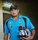 An Australian cricketer wearing blue jersey and carrying his helmet and gloves.