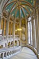 The principal staircase, Manchester Town Hall, with a spiral staircase projecting into it and typical Waterhouse glass and a painted ceiling of a blue sky with golden stars and suns on the vault. The staircase has stone steps and balustrade, the columns on the left allow natural light to flood into the corridor off which the major rooms of the building open, this is one of the most spatial complex designs of Waterhouse's career