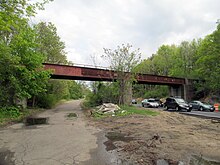A two-span girder railroad bridge over a section of highway. The left half of the road is disused.
