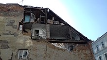 Old building on a street corner with a destroyed gable wall, revealing the insides of apartments.