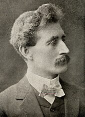 black and white right-face portrait of a man with bushy hair and moustache in formal attire