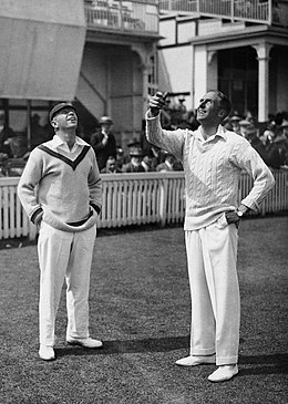 Photograph of Gilligan on the right, in front of fans, tossing a coin watched by South African Herbie Taylor on the left
