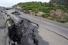 The remains of an asphalt road that has been destroyed with several pieces lifted up from the ground and others with large cracks.