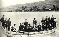 Pontian men wearing western suits in a canoe, Black Sea. Some wear fezes or carry instruments.