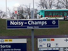 Sign indicating the name of the station (with a bus of line  213  in the background)