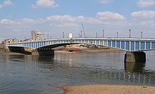 A long low bridge across a wide river. The bridge is painted in varying shades of blue, which render it hard to see against the water and sky.