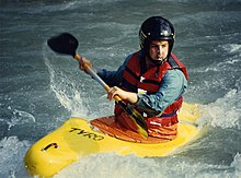 Photo of man in kayak holding paddle nearly parallel to the boat, surrounded by white water