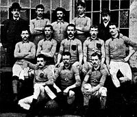 A group of thirteen men, eleven in association football attire typical of the late nineteenth century and two in suits and bowler hats.