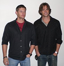 Two men wearing jeans and black shirts.