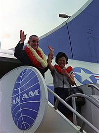 A photograph of a man and a woman wearing leis waving to the photographer standing on the landing of a Pan Am Airlines boarding ramp