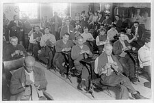 Group of prisoners seated, as they would be in a classroom, knitting socks for soldiers at Sing Sing, 1915