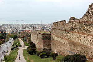 Photo of a medieval stone wall with towers, with a modern city and the sea in the background
