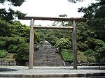 Stairs leading through a wooded area to a stone structure beyond a large torii.