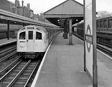 A westbound Piccadilly line train at Barons Court station, operated by a seven-car 1959 stock.