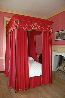 Four post bed surrounded by full set of bed hangings in a rich red fabric embroidered with gold, from a house in Colonial Williamsburg.