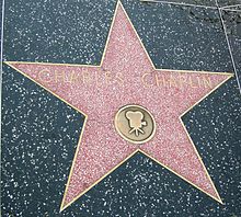 Farbfotografie in der Obersicht von einer Gehwegplatte mit einem rot-weiß gepunkteten Stern, der Gold umrandet ist. In goldener Schrift steht „Charles Chaplin“ und eine goldene Kamera ist in einem Kreis gemalt.