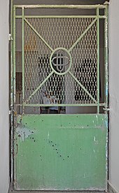 A jail door with a solid steel bottom and a grate on the top half