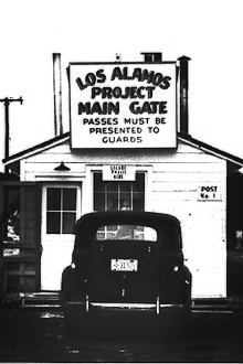 small guard shack with sign stating that passes must be presented to guards, a nineteen forties era car is parked there