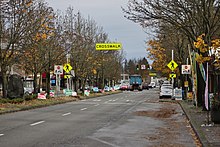 The view looking down a one-way street with two lanes and a pullout curb for parking. A crosswalk with signs and signals is seen at the center of the image, along with a line of political campaign signs.